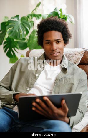 Zuversichtlicher Geschäftsmann, der den Laptop auf dem Klubsessel zurücklegt und zu Hause arbeitet Stockfoto