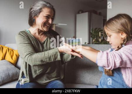 Glückliche Enkelin und Großmutter sitzen zu Hause auf dem Sofa Stockfoto
