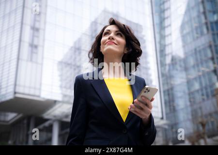 Lächelnde Geschäftsfrau, die aufblickt und ihr Smartphone hält Stockfoto