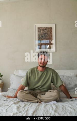 Ein lächelnder Mann sitzt zu Hause auf dem Bett Stockfoto