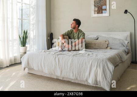 Nachdenklicher junger Mann, der zu Hause auf dem Bett sitzt Stockfoto