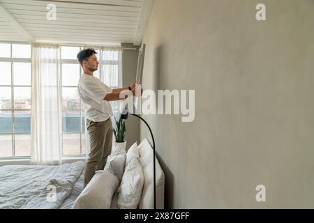 Mann hängt Bilderrahmen an der Wand im Schlafzimmer zu Hause Stockfoto