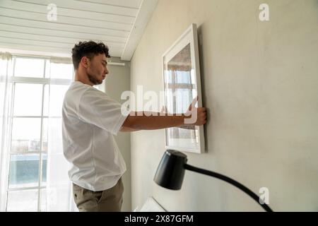 Ein Mann hängt zu Hause einen Bilderrahmen an die Wand Stockfoto