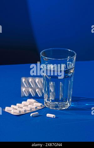 Pillen und ein Glas Wasser auf blauem Hintergrund Stockfoto