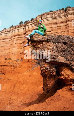 Reife Frau mit Rucksack sitzt auf Felsen am roten Canyon Stockfoto