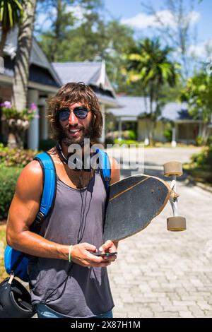 Bärtiger junger Mann mit Rucksack mit Longboard an sonnigen Tagen Stockfoto