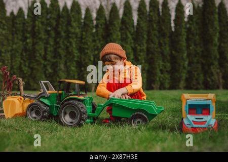 Junge hockt und spielt mit einem Spielzeugtraktor auf grünem Gras im Hinterhof Stockfoto