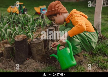 Junge hockt und tränkt Blumen aus der Dose im Garten Stockfoto