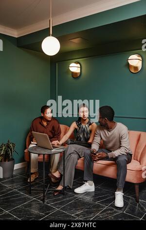 Verschiedene Kollegen diskutieren über Laptop, der im Büro auf dem Sofa sitzt Stockfoto