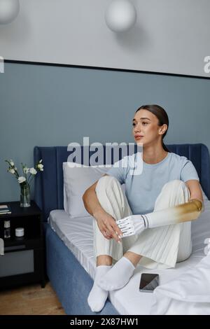Nachdenkliche junge Frau mit Armprothese, die auf dem Bett sitzt Stockfoto