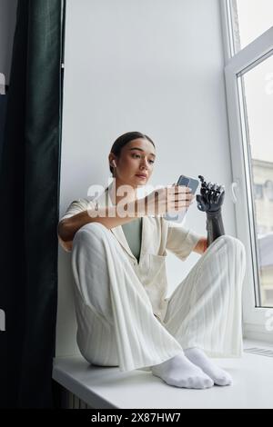 Entspannte Frau mit Armprothese, die Musik hört, die auf der Fensterbank sitzt Stockfoto