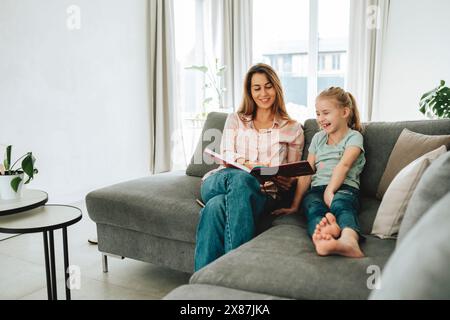 Lächelnde Tochter und Mutter lesen zu Hause Buch Stockfoto