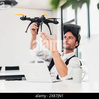 Reifer Geschäftsmann, der eine VR-Brille trägt und Drohne am Schreibtisch im Büro untersucht Stockfoto