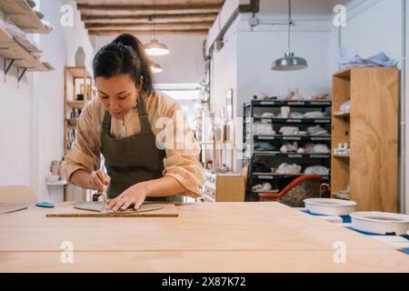 Geschickter Handwerker, der Ton auf dem Tisch formt, am Keramikarbeitsplatz Stockfoto