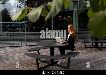 Junge rothaarige Geschäftsfrau, die mit Laptop im Büropark sitzt Stockfoto