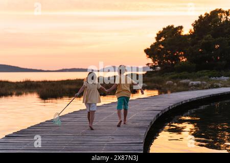 Bruder und Schwester mit Fischernetz, das bei Sonnenaufgang auf dem Pier über dem See läuft Stockfoto