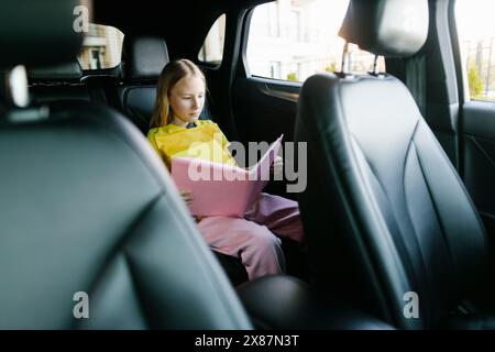 Ein fokussiertes Mädchen liest Buch auf dem Rücksitz des Autos Stockfoto