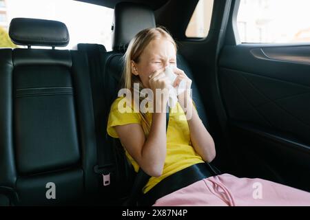Das kranke Mädchen niest auf dem Rücksitz des Autos Stockfoto