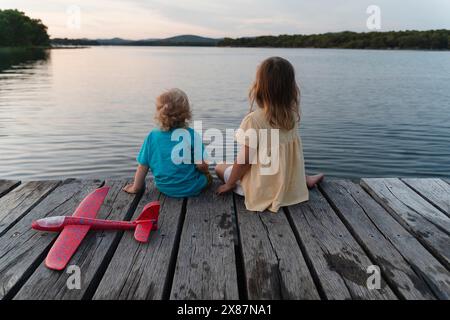 Bruder und Schwester sitzen auf dem Pier über dem See Stockfoto