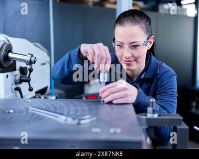 Ingenieur trägt Schutzbrille und misst Werkstück im Werk Stockfoto