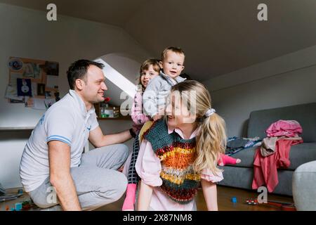 Lächelnder Mann von Kindern auf dem Rücken der Mutter im Wohnzimmer Stockfoto