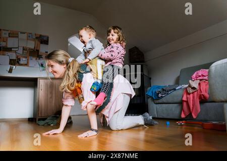 Glückliche Mutter mit Kindern auf dem Rücken im Wohnzimmer Stockfoto