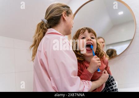 Mädchen putzt Zähne von Mutter im Badezimmer Stockfoto