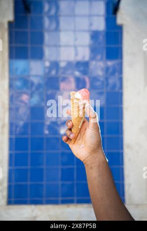 Ein Mann hält einen schmelzenden Eiskegel vor einer blauen Wand Stockfoto