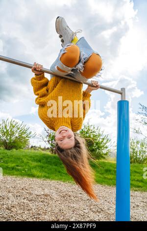 Fröhliches Mädchen, das kopfüber an der Turnbar auf dem Spielplatz hängt Stockfoto