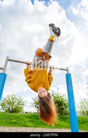 Glückliches Mädchen, das kopfüber an der Turnbar auf dem Spielplatz hängt Stockfoto