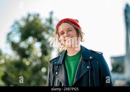 Lächelnde junge Frau mit Strickmütze und Lederjacke Stockfoto
