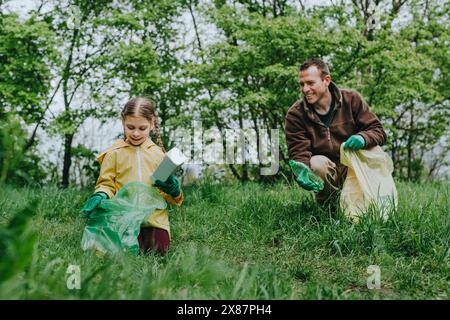 Lächelnder Vater und Tochter sammeln Plastikflaschen im Wald Stockfoto