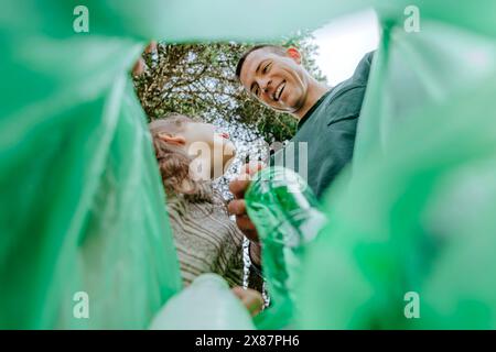 Glücklicher Vater und Tochter sammeln Plastikflaschen in Müllsack Stockfoto