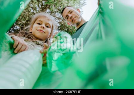 Lächelnder Vater und Tochter sammeln Plastikflaschen in Müllsack Stockfoto