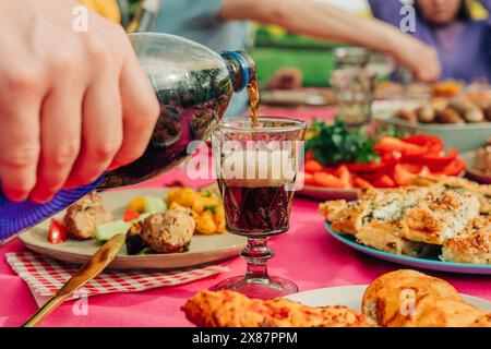 Hand eines Mannes, der kaltes Getränk in Glas am Tisch gießt Stockfoto