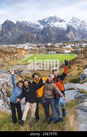 Norwegen, Nordnorwegen, Henningsvaer, Gruppe von Freunden posiert in Lofoten mit Fußballfeld im Hintergrund Stockfoto