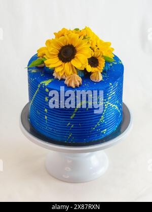 Atemberaubender Kuchen mit hellblauer Glasur, verziert mit frischen Sonnenblumen und Feigen, auf einem weißen Kuchenständer vor neutralem Hintergrund Stockfoto