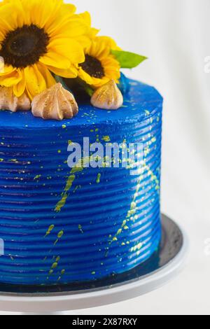 Atemberaubender Kuchen mit hellblauer Glasur, verziert mit frischen Sonnenblumen und Feigen, auf einem weißen Kuchenständer vor neutralem Hintergrund Stockfoto