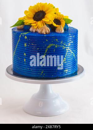 Atemberaubender Kuchen mit hellblauer Glasur, verziert mit frischen Sonnenblumen und Feigen, auf einem weißen Kuchenständer vor neutralem Hintergrund Stockfoto