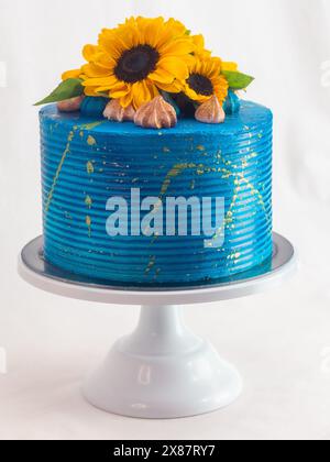 Atemberaubender Kuchen mit hellblauer Glasur, verziert mit frischen Sonnenblumen und Feigen, auf einem weißen Kuchenständer vor neutralem Hintergrund Stockfoto