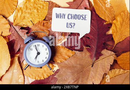 Eine Uhr steht auf einem Stapel Blätter mit den Worten Warum wählen Sie uns Stockfoto