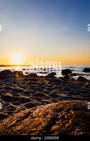 Die Sonne sinkt langsam unter den Horizont und wirft ein warmes Nachglühen über dem ruhigen Gewässer. Der Himmel ist mit Rot- und Orang-Tönen bemalt Stockfoto