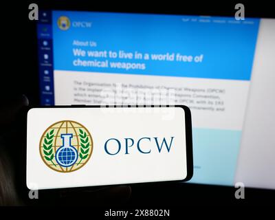 Person, die ein Smartphone mit dem Logo der Organisation für das Verbot chemischer Waffen (OVCW) vor der Website hält. Schwerpunkt auf dem Display des Telefons. Stockfoto