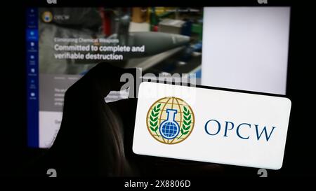 Person, die ein Mobiltelefon mit dem Logo der Organisation für das Verbot chemischer Waffen (OVCW) vor der Webseite hält. Schwerpunkt auf dem Display des Telefons. Stockfoto