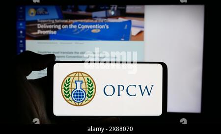 Person, die ein Mobiltelefon mit dem Logo der Organisation für das Verbot chemischer Waffen (OVCW) vor der Webseite hält. Schwerpunkt auf dem Display des Telefons. Stockfoto