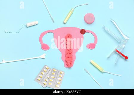 Papieruterus mit gynäkologischem Spekulum, Pillen und Tampons auf blauem Hintergrund Stockfoto