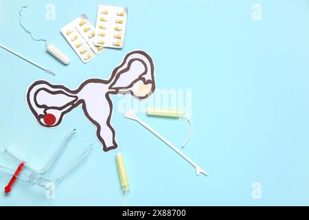 Papieruterus mit gynäkologischem Spekulum, Pillen und Tampons auf blauem Hintergrund Stockfoto