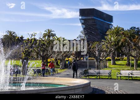 San Francisco, CA, USA. 30. März 2024 : Eine ruhige Szene vor dem de Young Museum mit einem lebhaften Brunnen und üppigen tropischen Bäumen. Stockfoto