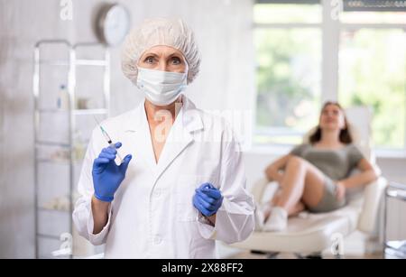 Ältere Ärztin in Maske mit Spritze Stockfoto
