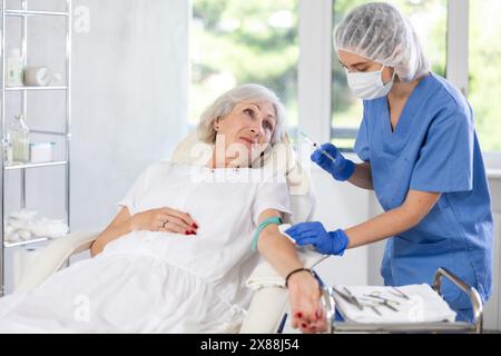 Weibliche Ärztin, die der schläfrigen, müden alten Frau in der Klinik eine Injektion gibt. Stockfoto